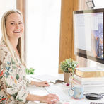 Sara Dunn of Sara Does SEO in a light office with windows sitting in front of a mac computer