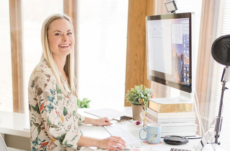 Sara Dunn of Sara Does SEO in a light office with windows sitting in front of a mac computer