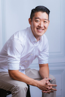 Man sitting down smiling and leaning forward with hands crossed, studio corporate photoshoot