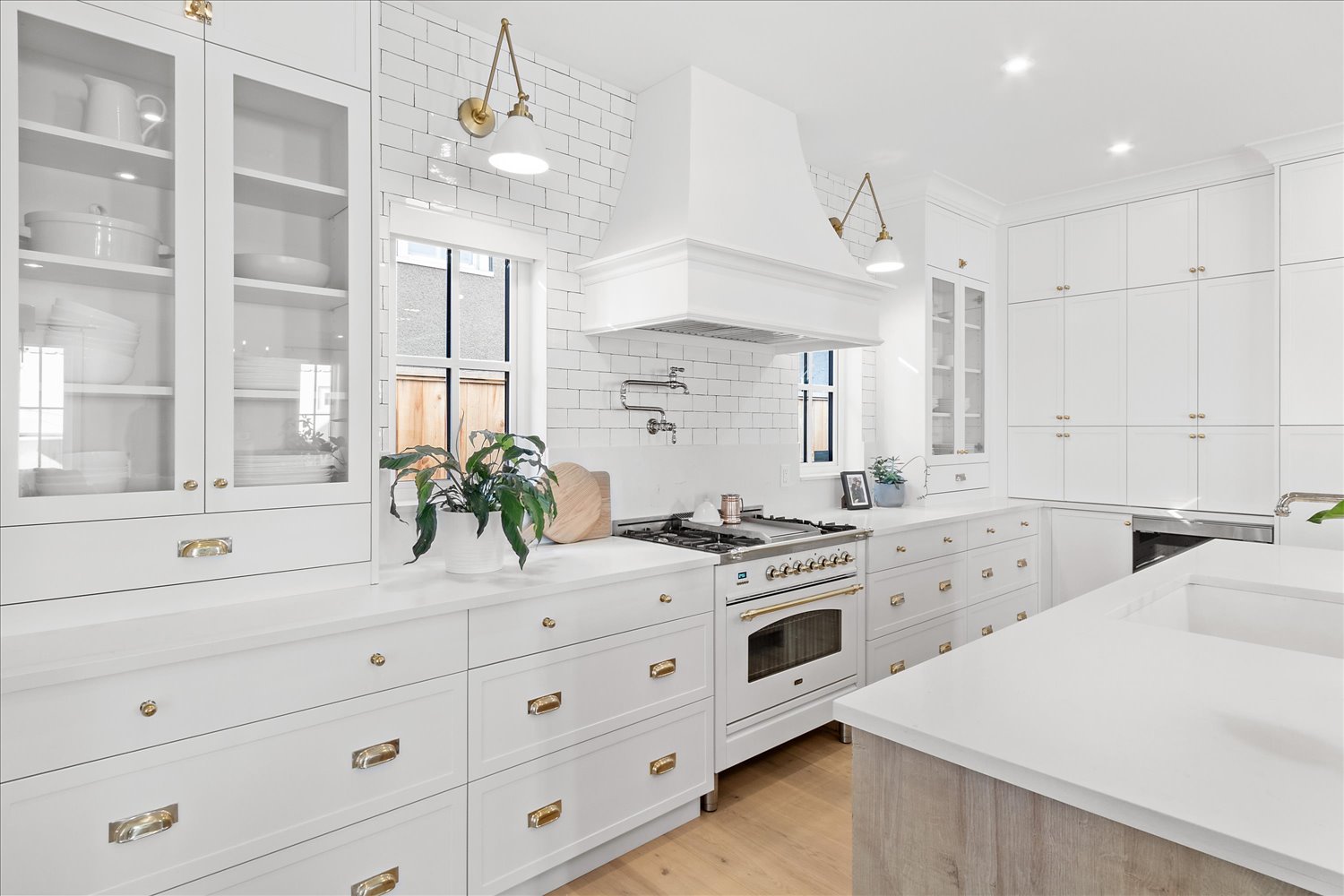 A luxury kitchen showcasing white custom cabinets with gold accents, a built-in gas range, and a vent hood framed by a tiled 