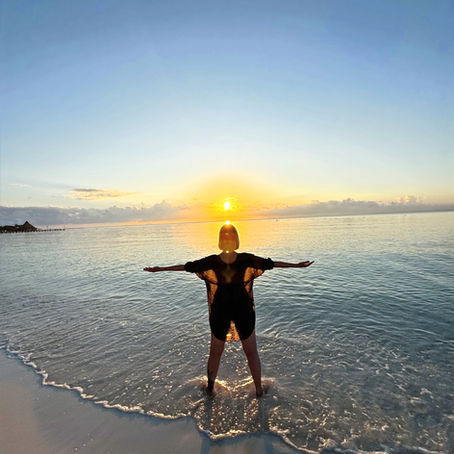 woman standing in the ocean at sunrise with open arms symbolizing balance between feminine and masculine energy