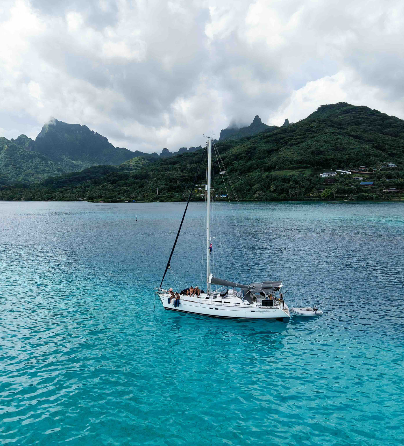A cruising yacht at anchor in clear turquoise water off a green headland.