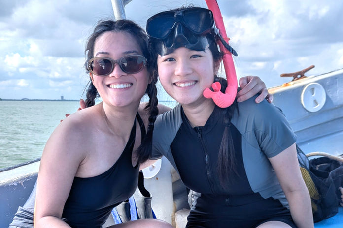 Two women in swimsuits, smiling on a boat with a snorkel. The background shows a cloudy sky and water. Bright, happy mood during a Cancun snorkel trip.