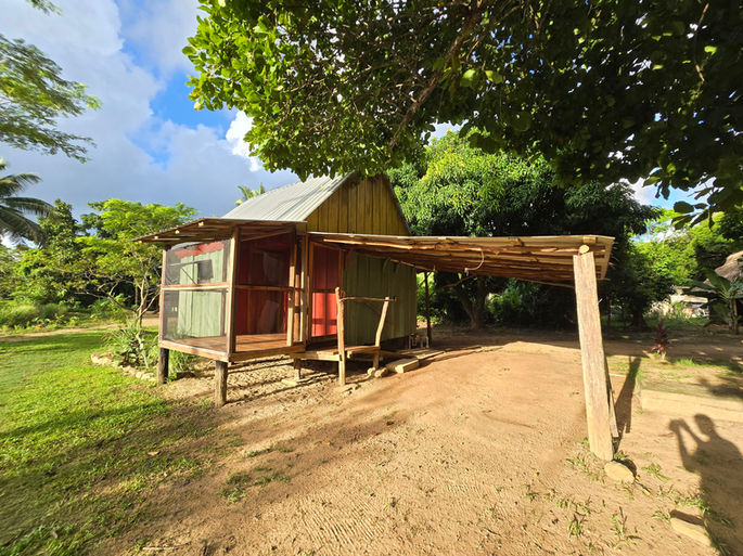 Small rustic cottage with a covered porch surrounded by green trees