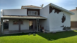 Casa residencial branca com pintura descascada e escada, em reforma.