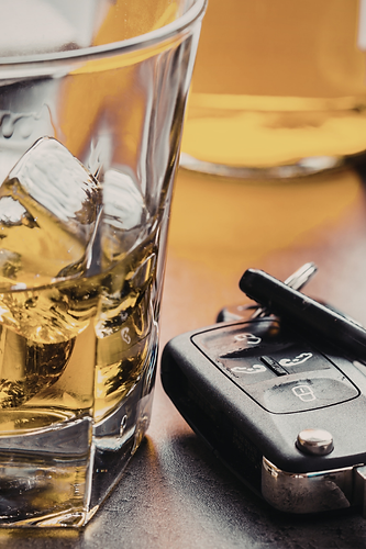 Glass with whisky and ice with a car key next to it