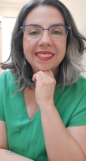 Uma foto minha, foco no rosto: mulher branca, com cabelos grisalhos, com o queixo apoiado na mão, sorrindo.