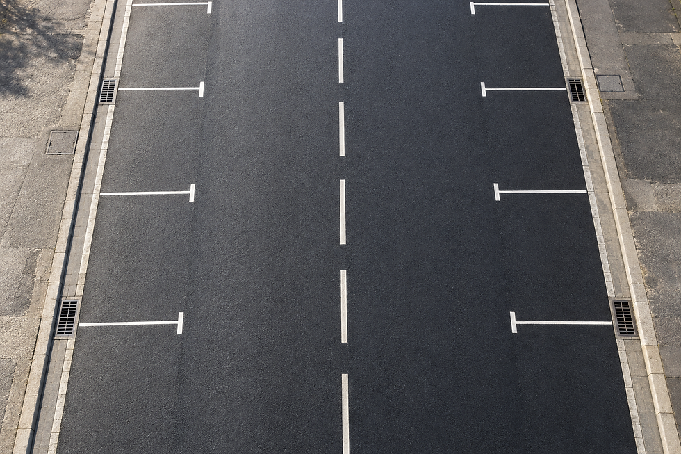Empty parking spaces line both sides of a freshly paved road with centre markings.
