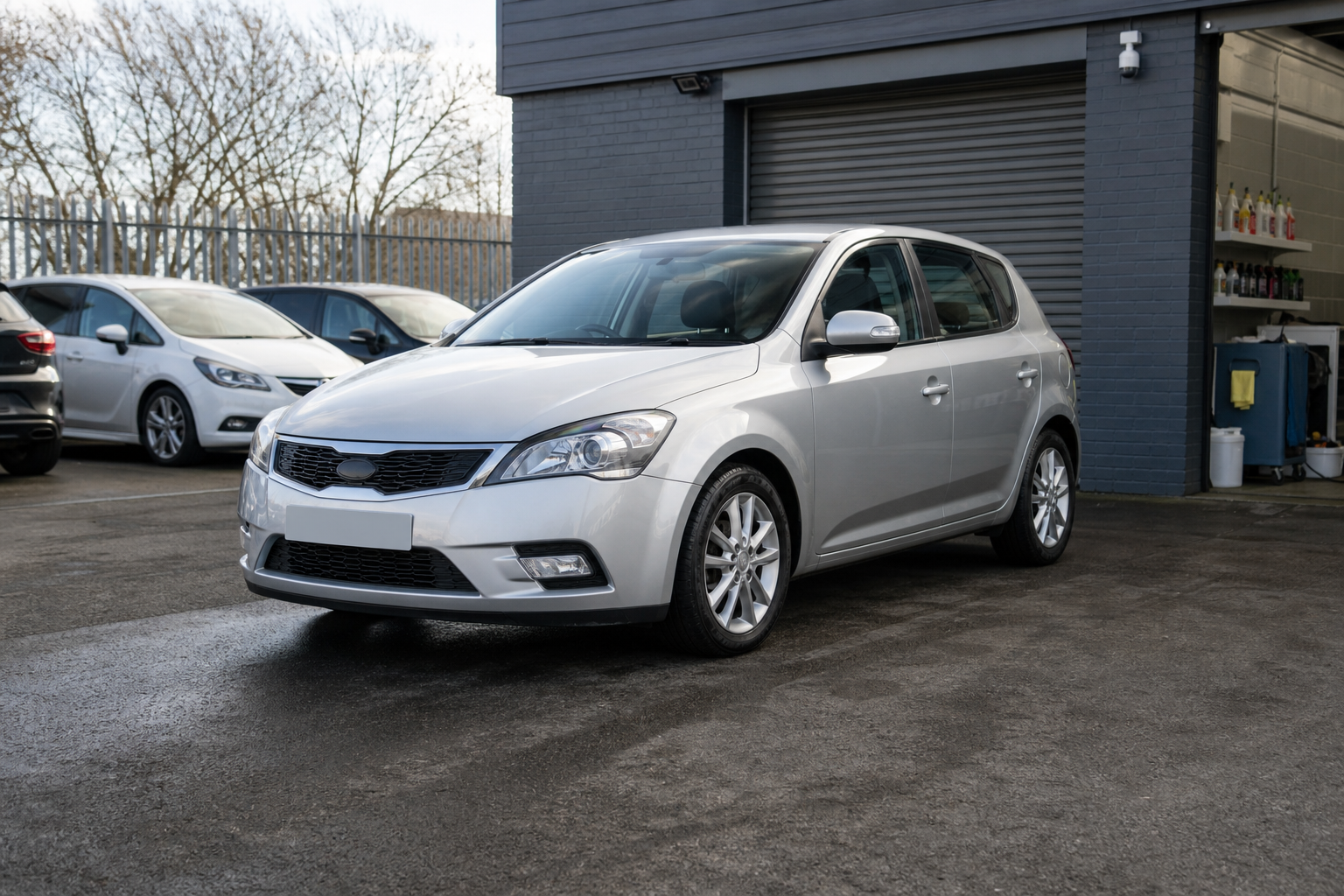 Silver hatchback car parked outside a garage on a cloudy day.