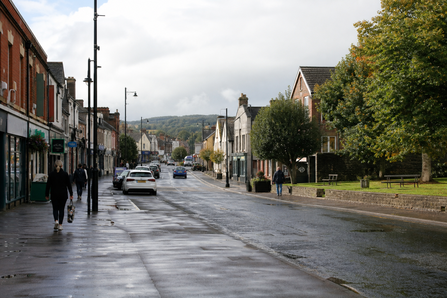 A quiet street with wet pavement, lined with shops and trees, under a cloudy sky.