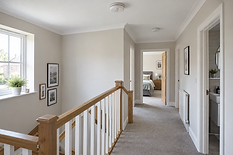 Upstairs hallway with cream walls, light carpet, and a view into a bedroom featuring a neatly made bed.