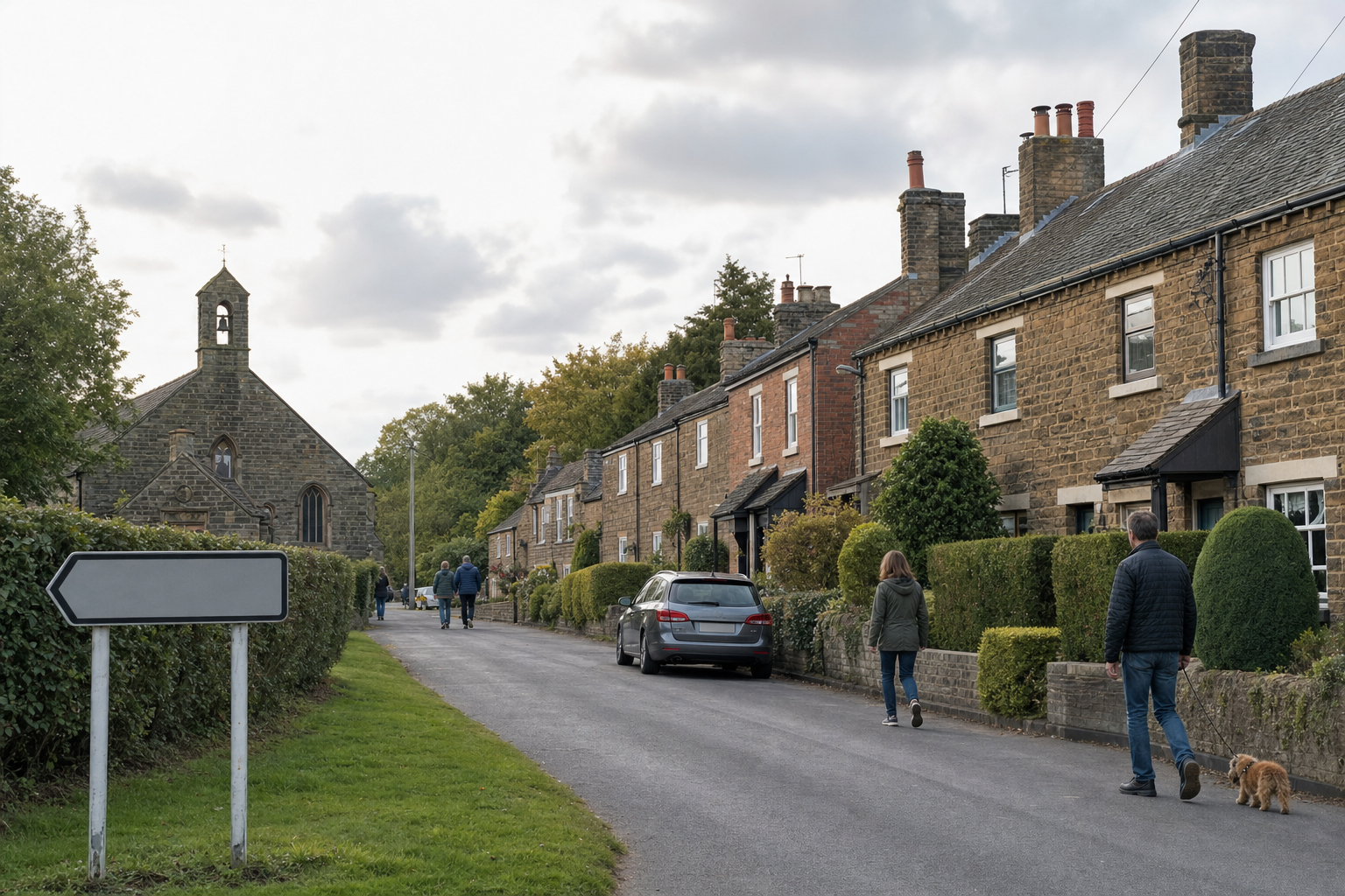 A village street with stone houses and a church, featuring people walking and a parked car.