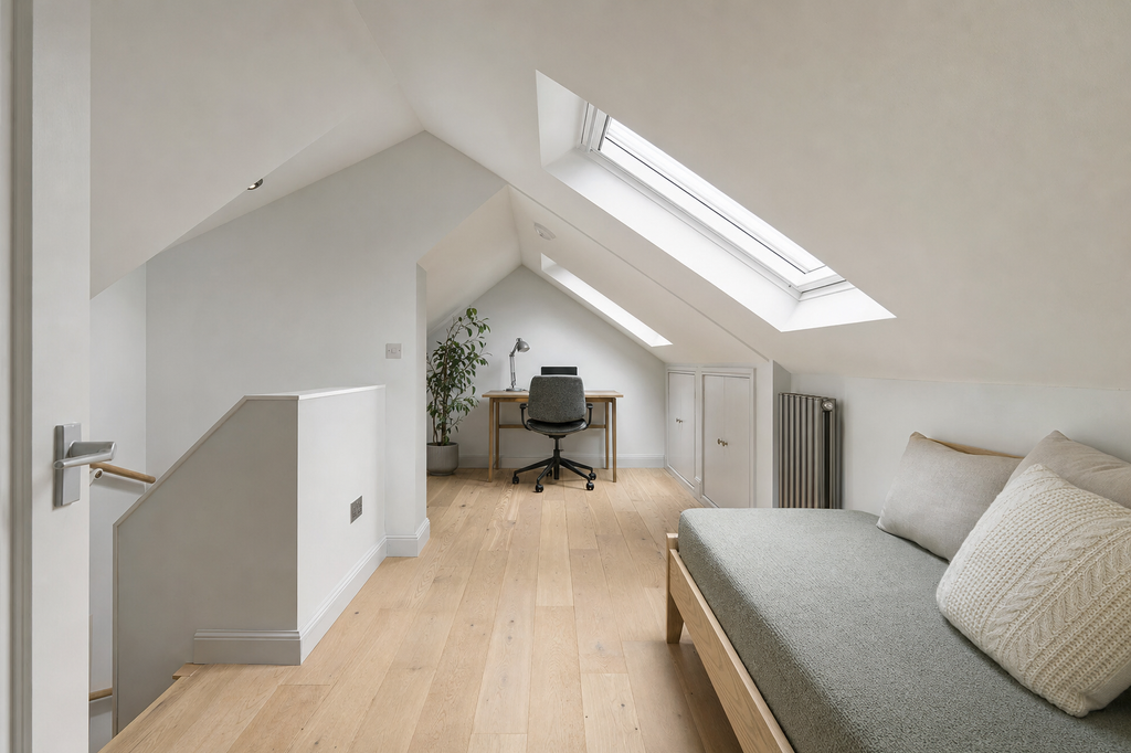 A cosy attic office with skylights, featuring a desk, office chair, potted plant, and daybed with cushions.