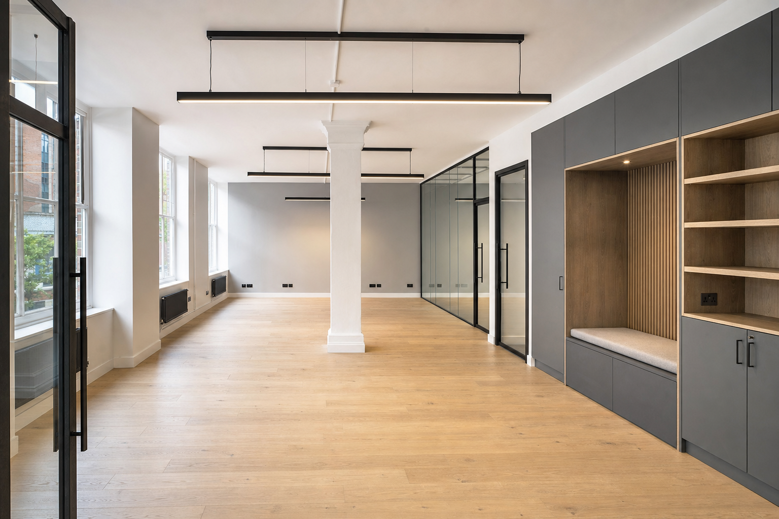 Modern open-plan office with wooden flooring, large windows, and glass partitions.