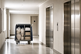 A linen trolley filled with pillows, sheets, and towels stands in a hotel corridor near lift doors.