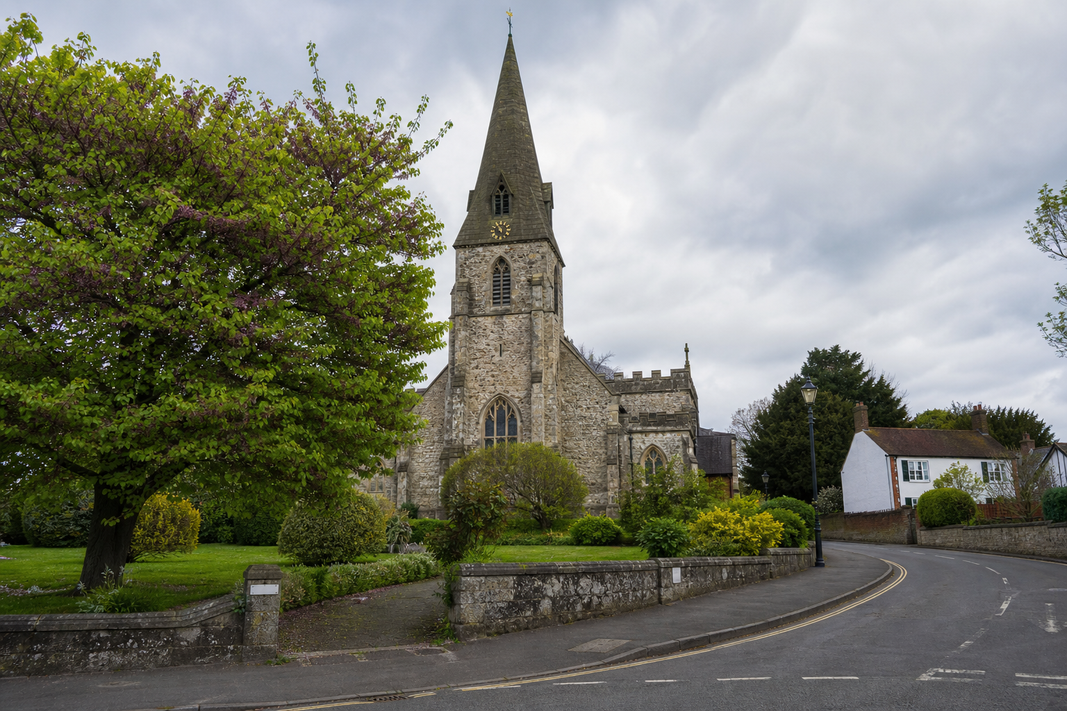 Stone church with a tall spire surrounded by lush greenery and a curved road.