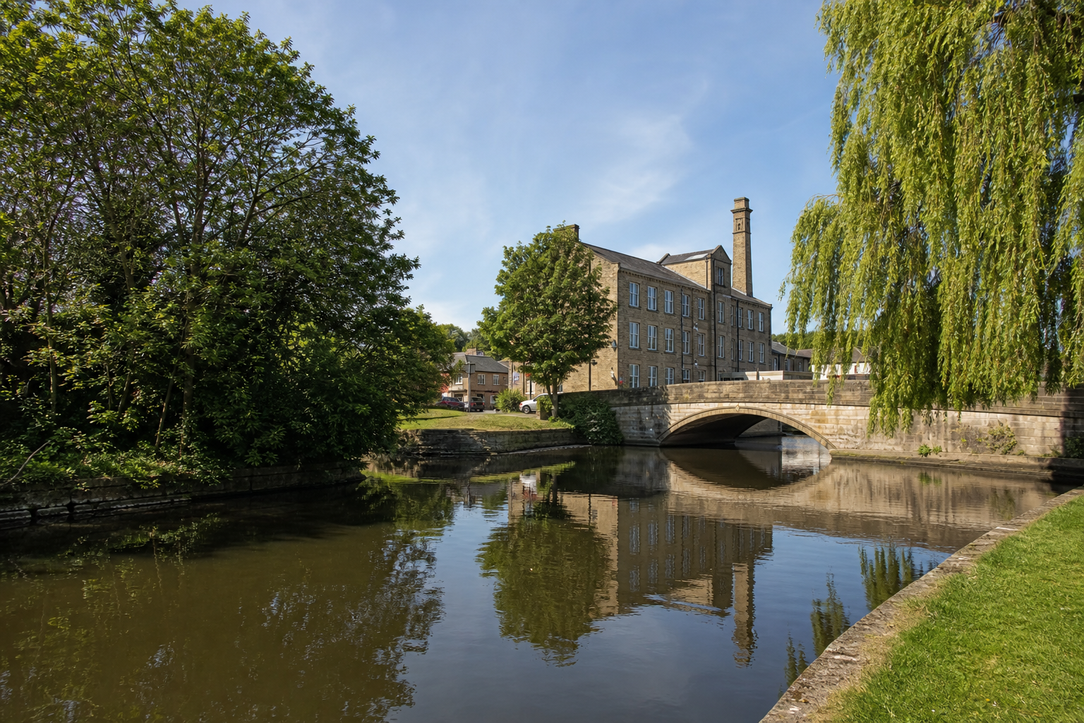 A historic stone building and arched bridge are reflected in a calm river.