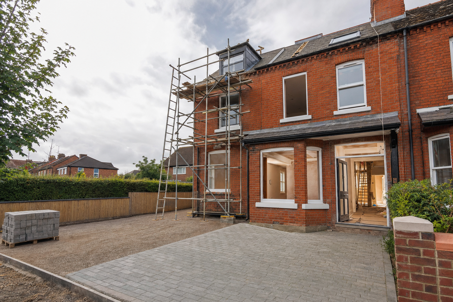 Red brick house undergoing renovation with scaffolding and an unfinished driveway.