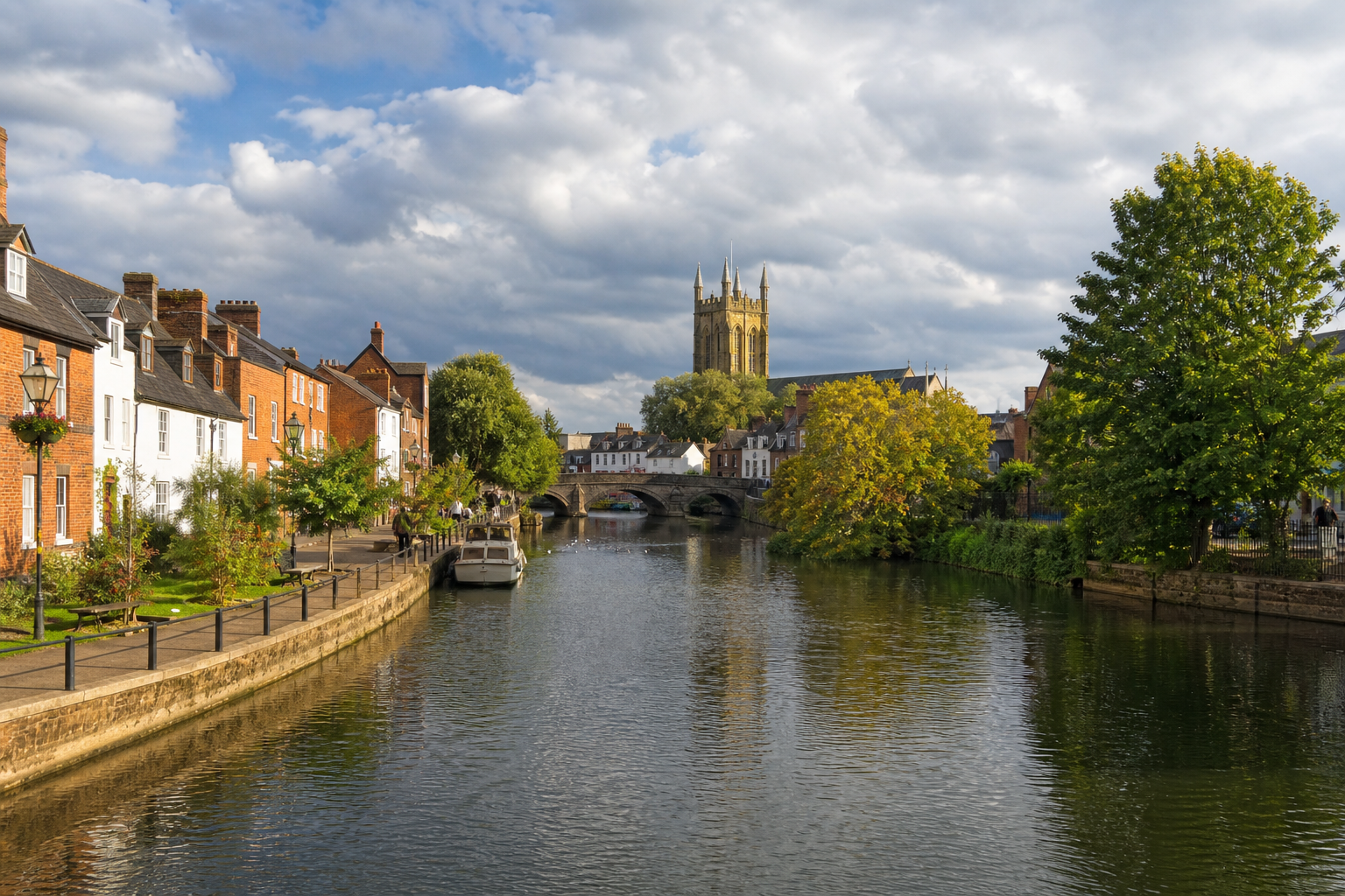 A serene riverside scene with a stone bridge and historic buildings under a partly cloudy sky.