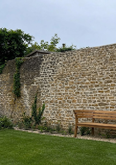 Wooden garden bench against a tall stone wall with climbing ivy