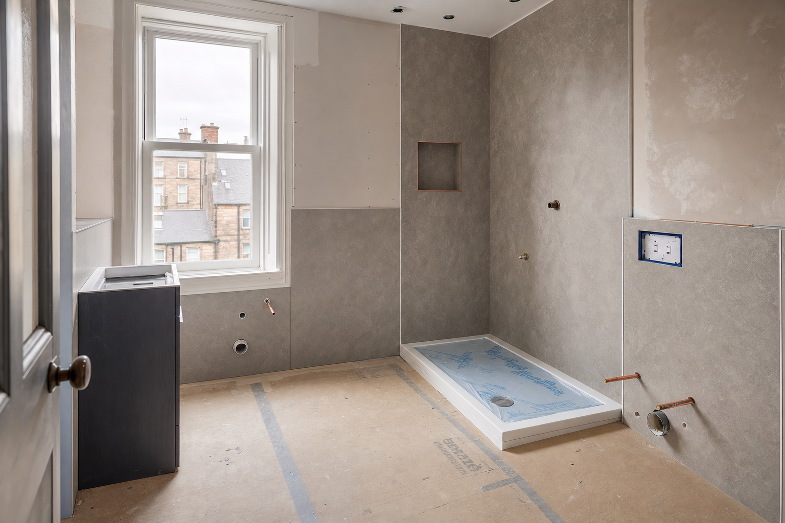 Unfinished bathroom being renovated, featuring a window, shower base, and plumbing work in progress.