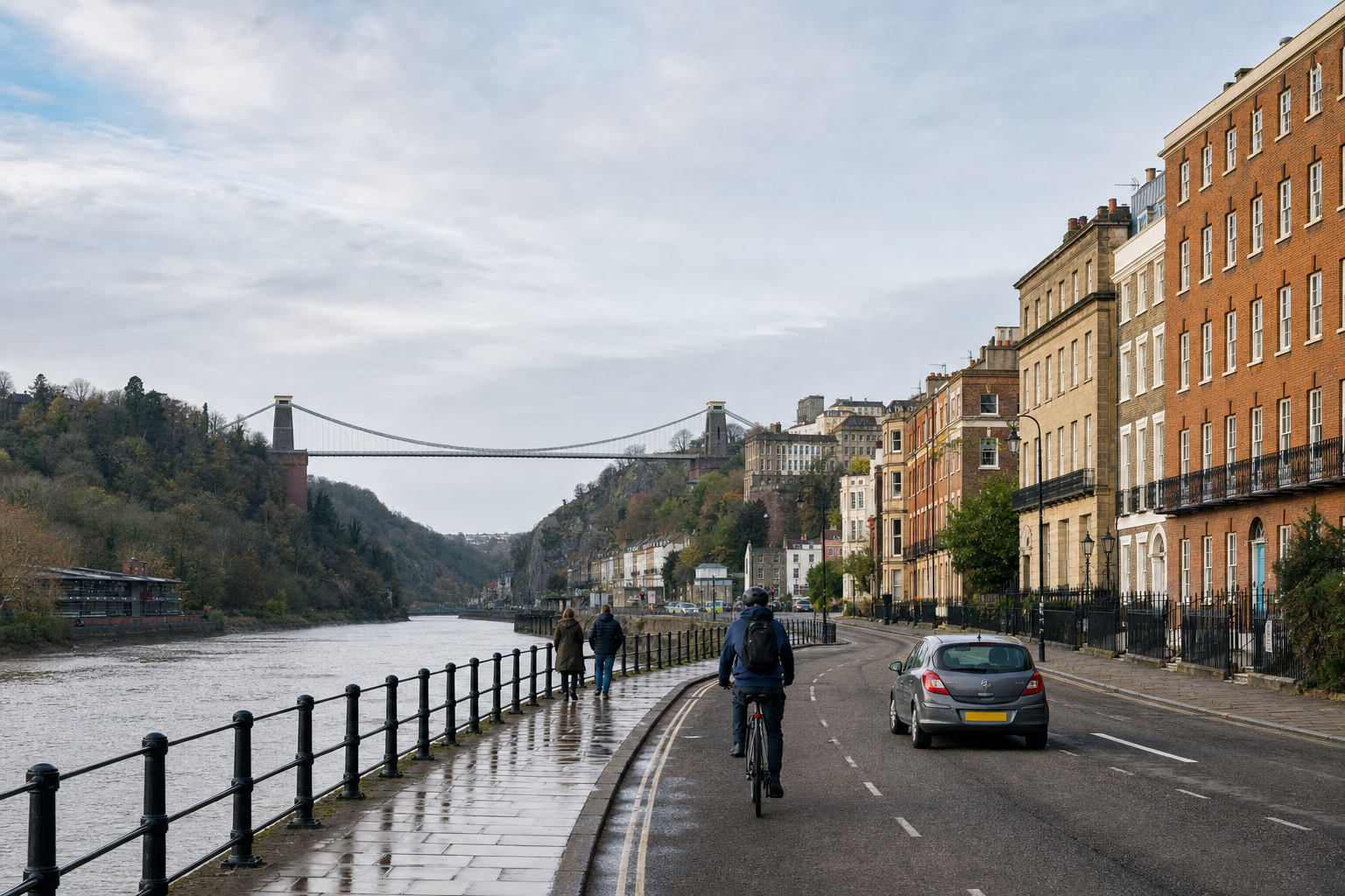 Cyclist and pedestrians on a riverside road with the Clifton Suspension Bridge in the distance.