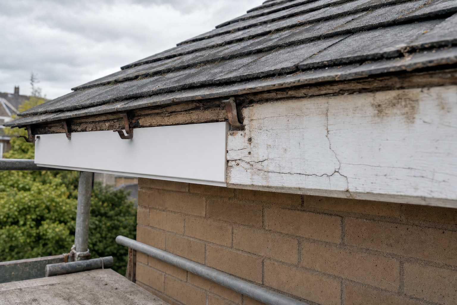A cracked and weathered soffit board beneath a tiled roof with a scaffold for maintenance.