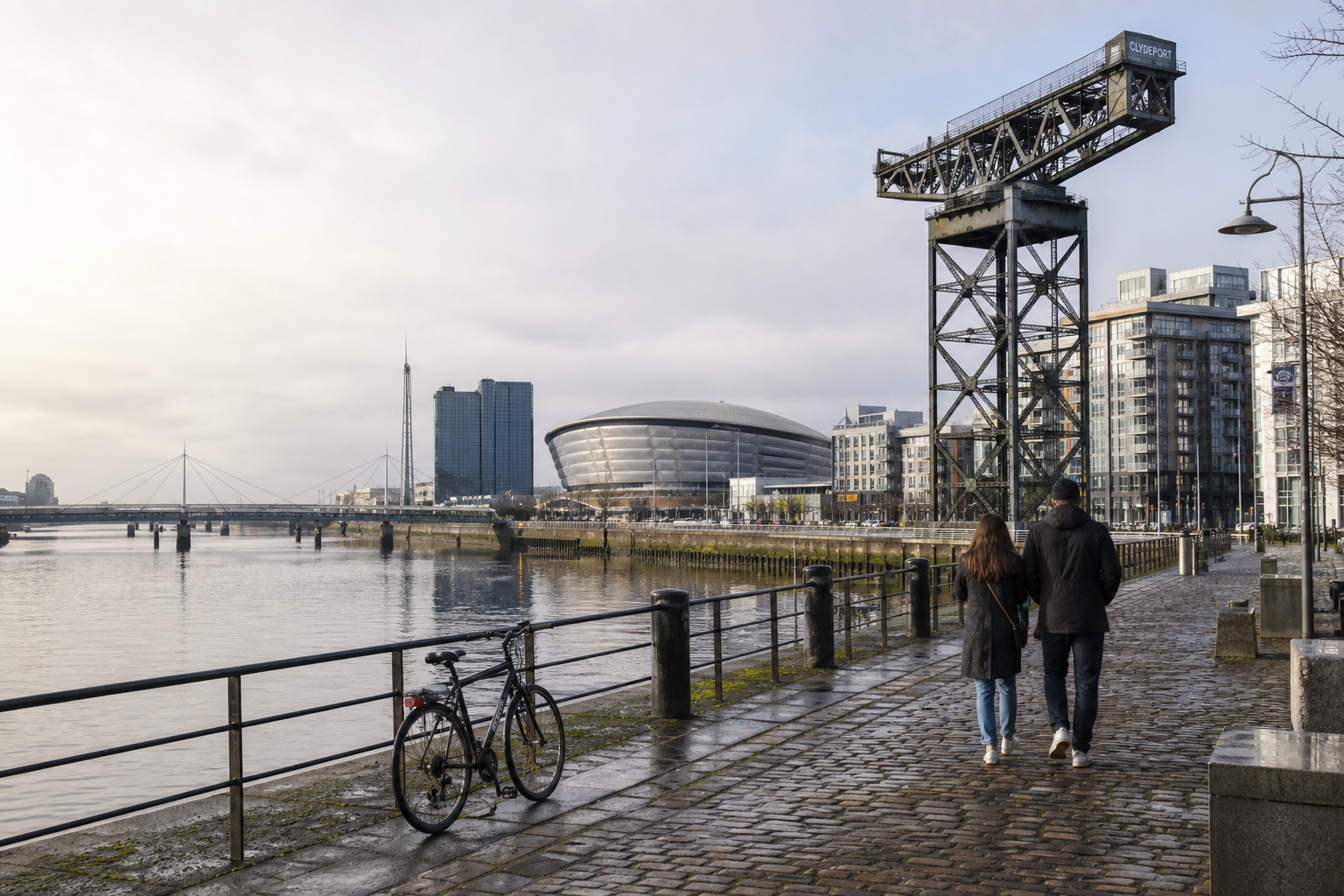 Couple walking along a riverside path next to a bicycle, with modern buildings and an old crane in the background.