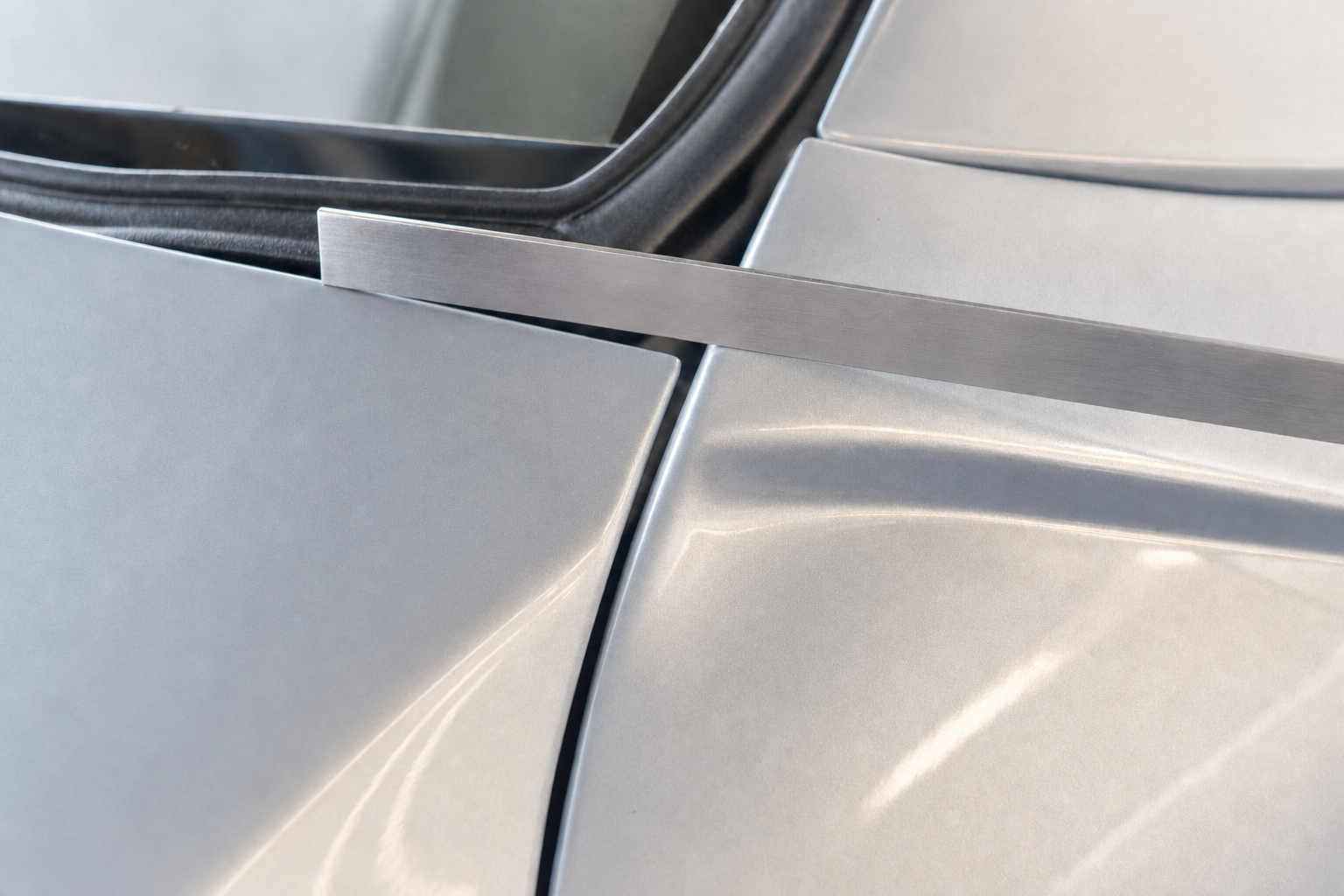 A metal strip aligns with a gap between two panels on a silver vehicle.