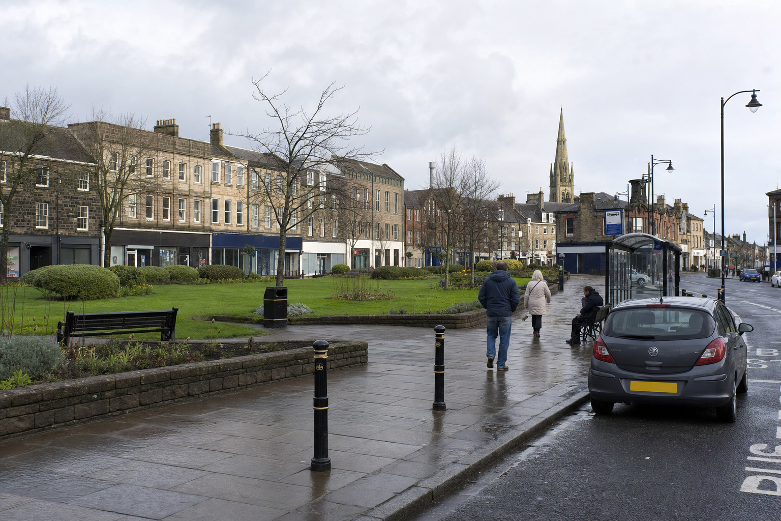 People walking along a wet pavement beside parked cars and shops in a town centre with a church spire in the background.