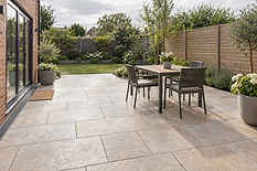 A modern patio with a wooden table, chairs, and potted plants overlooking a garden with trees and flowers.