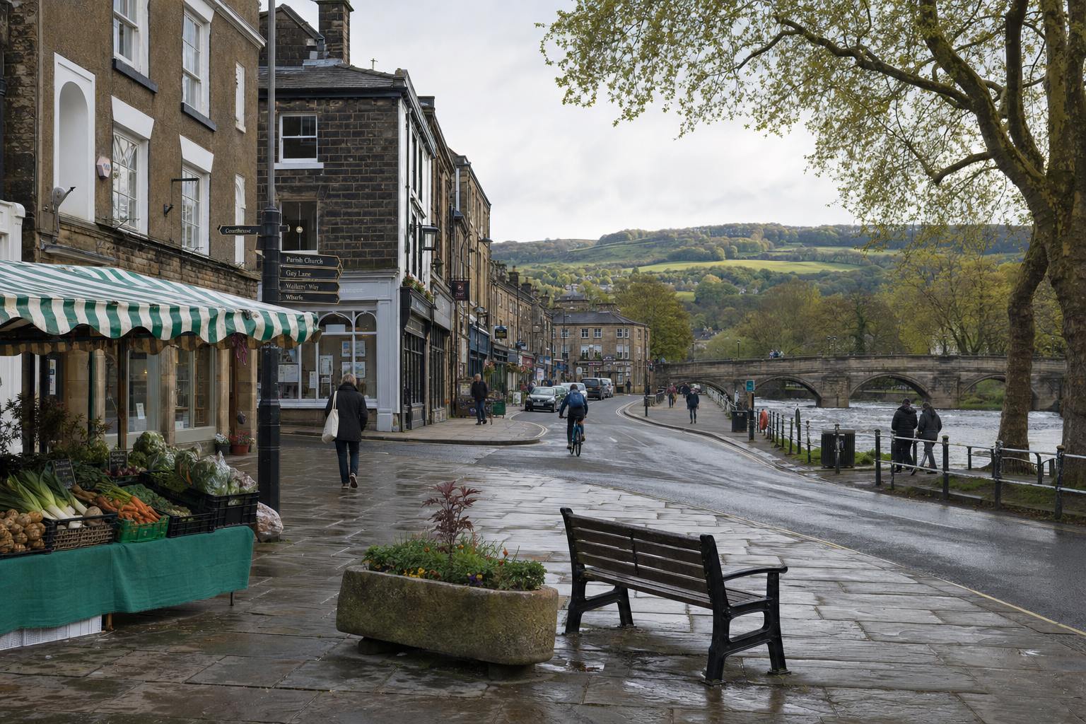 A bustling market street beside a river with a stone bridge and distant hills under a cloudy sky.