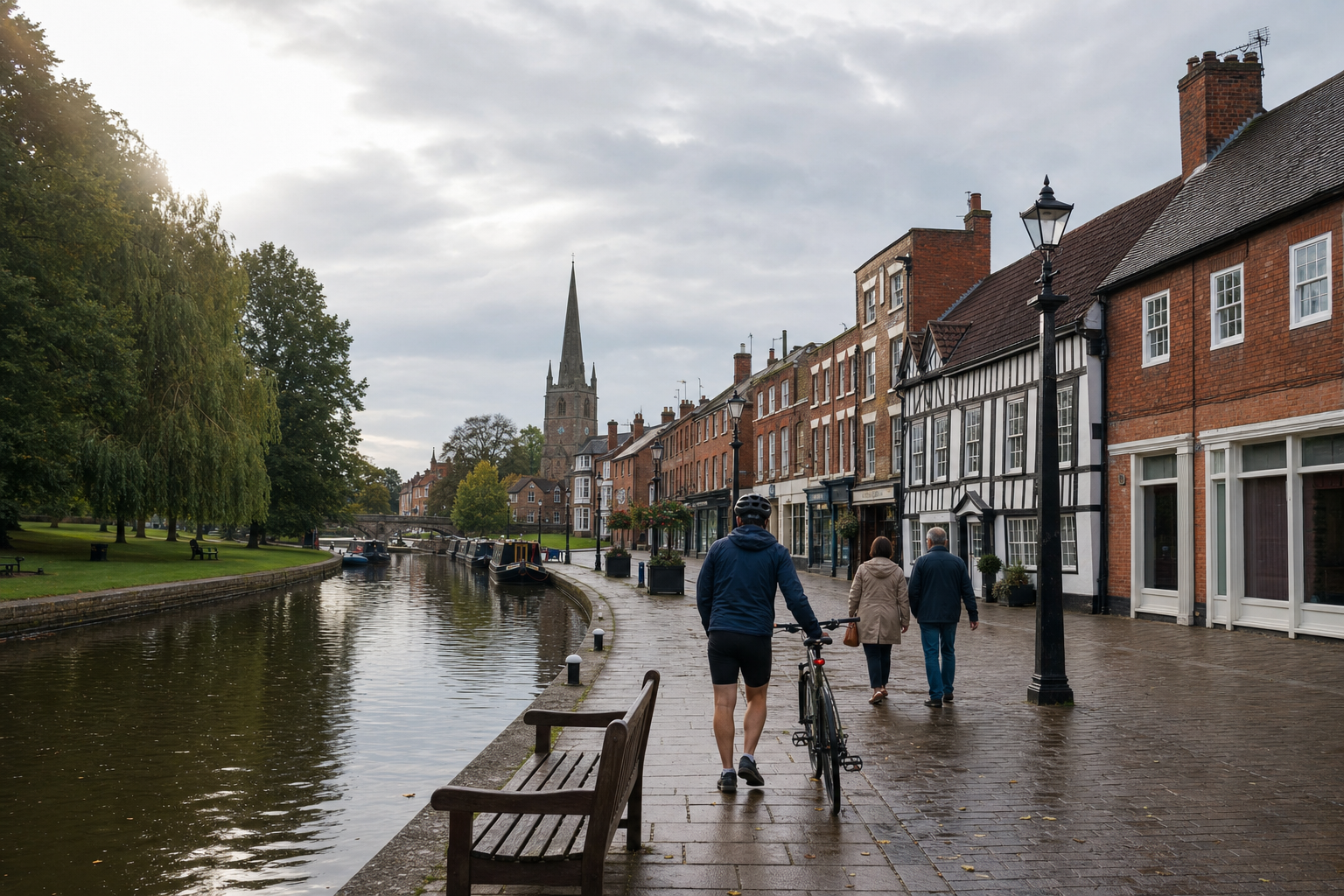 A cyclist walks alongside a canal with boats, flanked by historic buildings and a prominent church spire in the background.