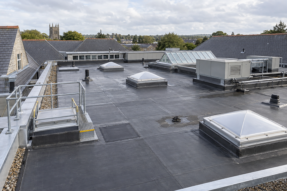 Flat commercial rooftop with skylights and ventilation units, surrounded by slate roofs and a distant church spire.