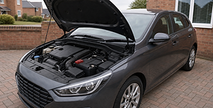 A grey hatchback parked on a driveway with the bonnet open, revealing the engine compartment.