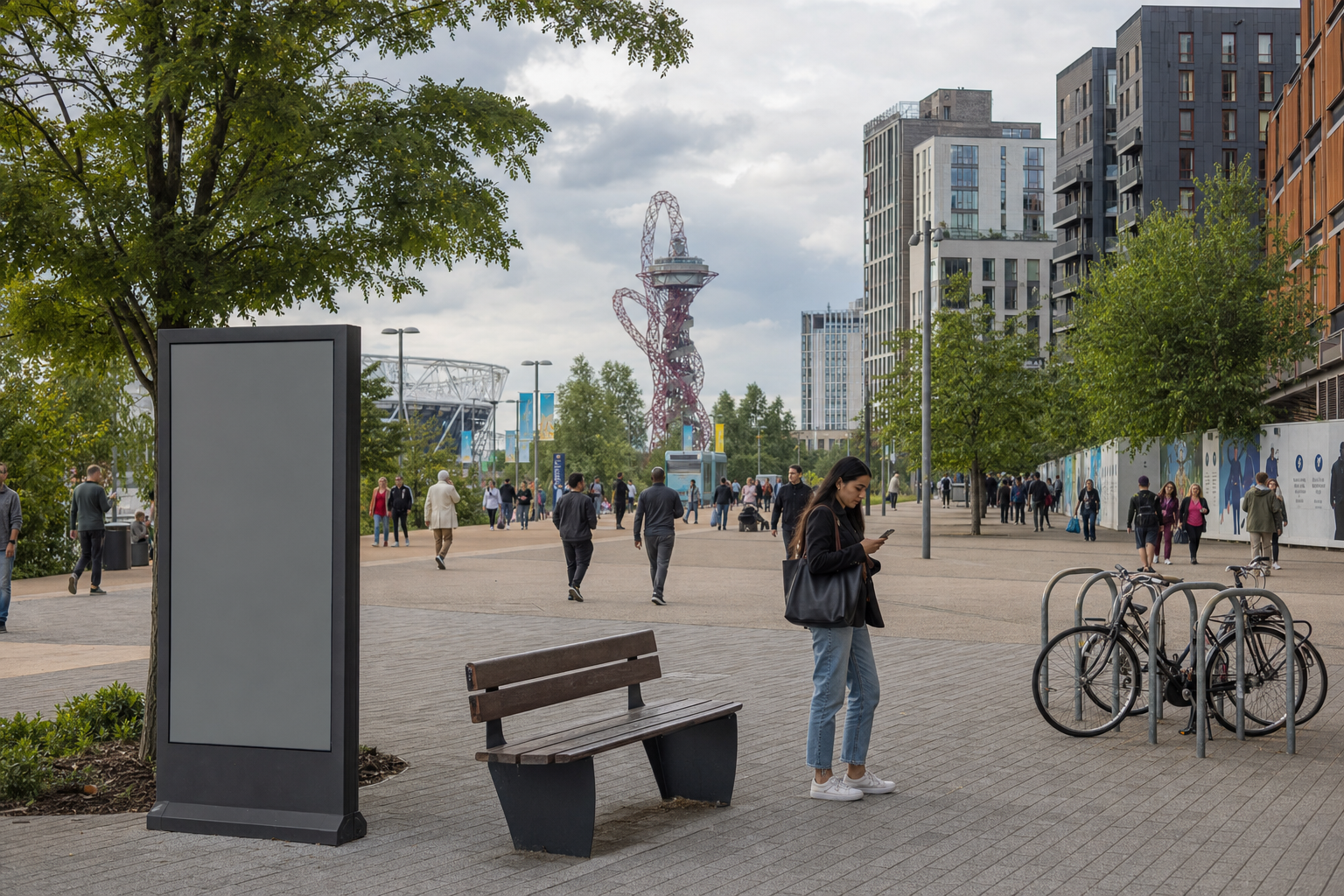 People walking in an urban park with a woman using her phone near a bench and bicycles.