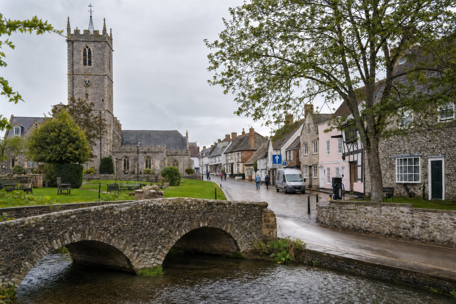 A stone church overlooks a quaint village street with historic buildings and a stone bridge over a small stream.