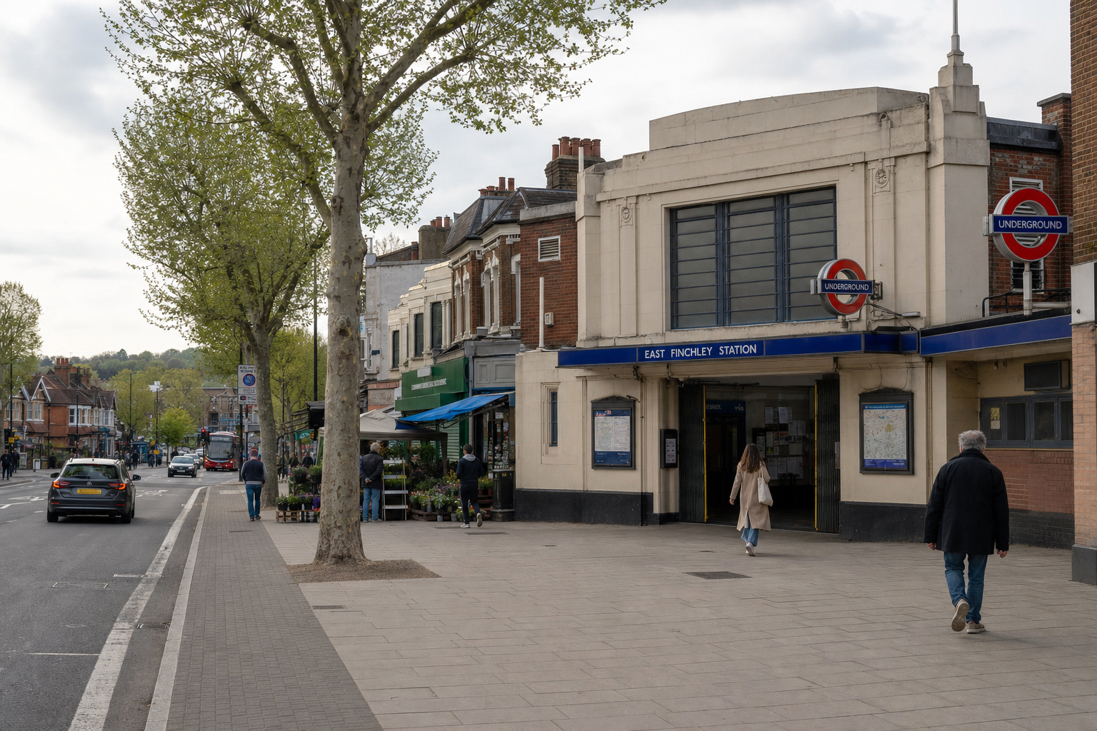 East Finchley Underground Station entrance with pedestrians, a tree-lined street, and nearby shops visible.