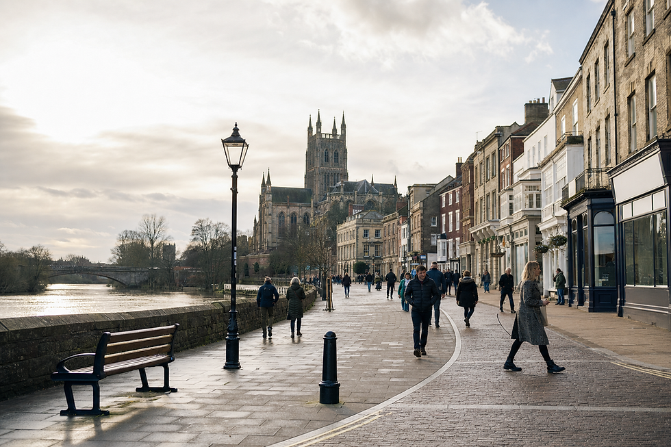 People walking along a riverside promenade with historical buildings and a large cathedral in the background.