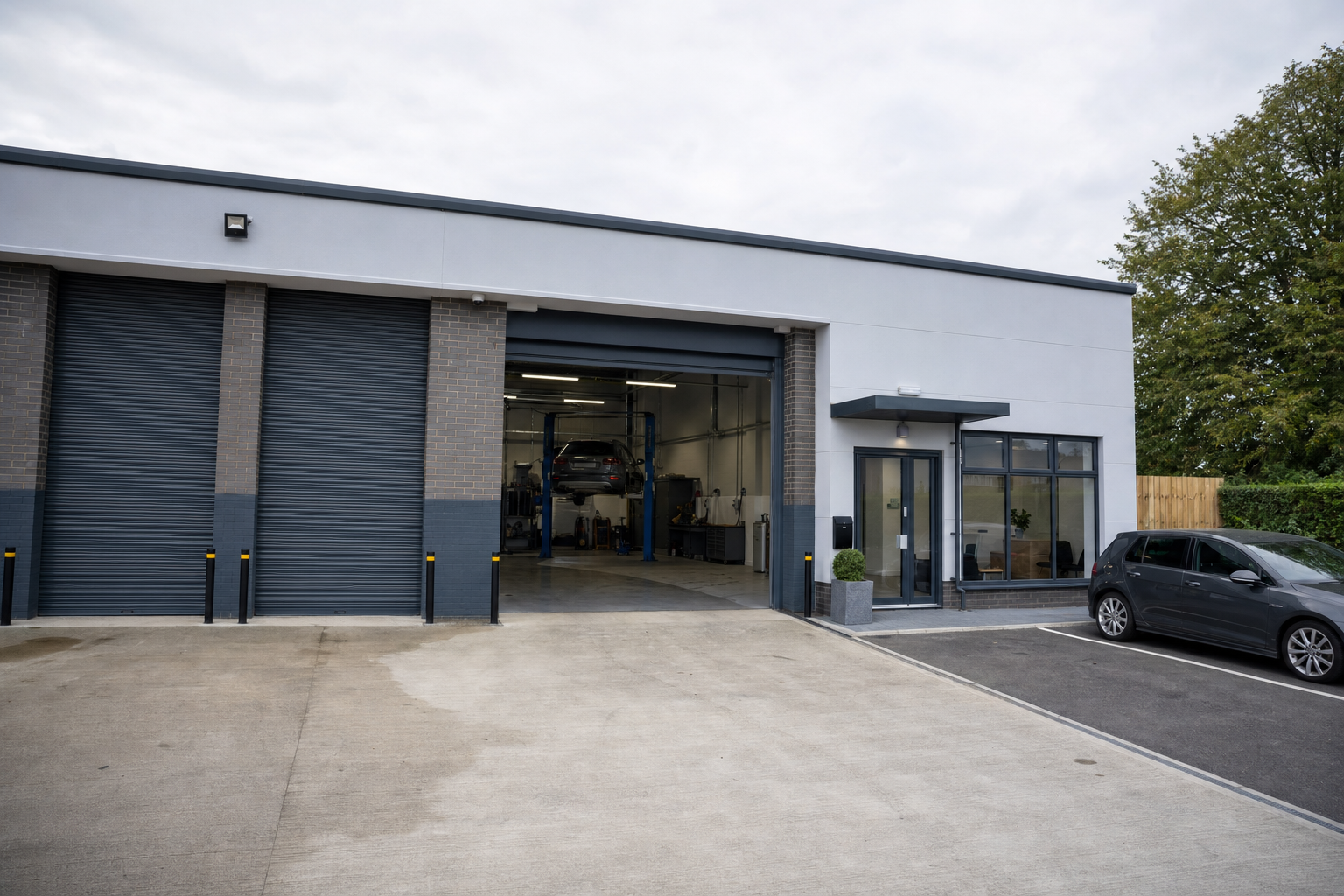 Car workshop with open garage, vehicle on lift, and adjacent office in a modern industrial building.
