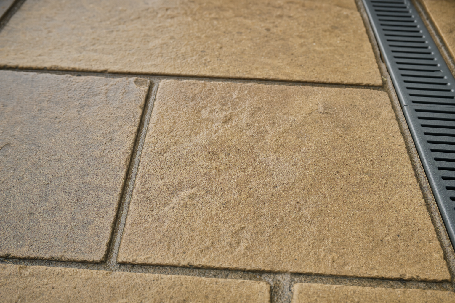 Close-up of textured stone paving slabs next to a metal drainage grate.