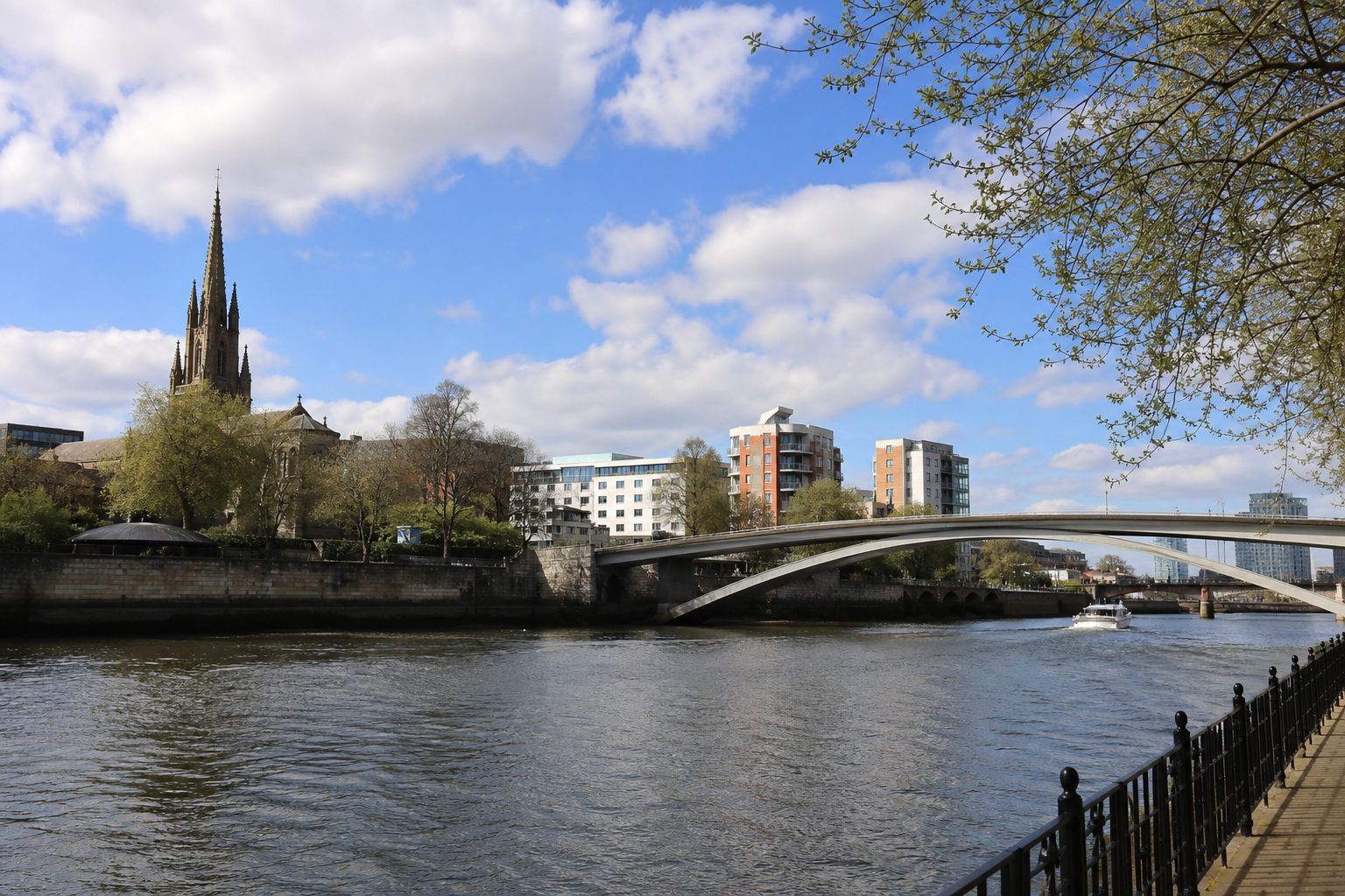 River scene with a church, modern buildings, a bridge, and a boat under a partly cloudy sky.