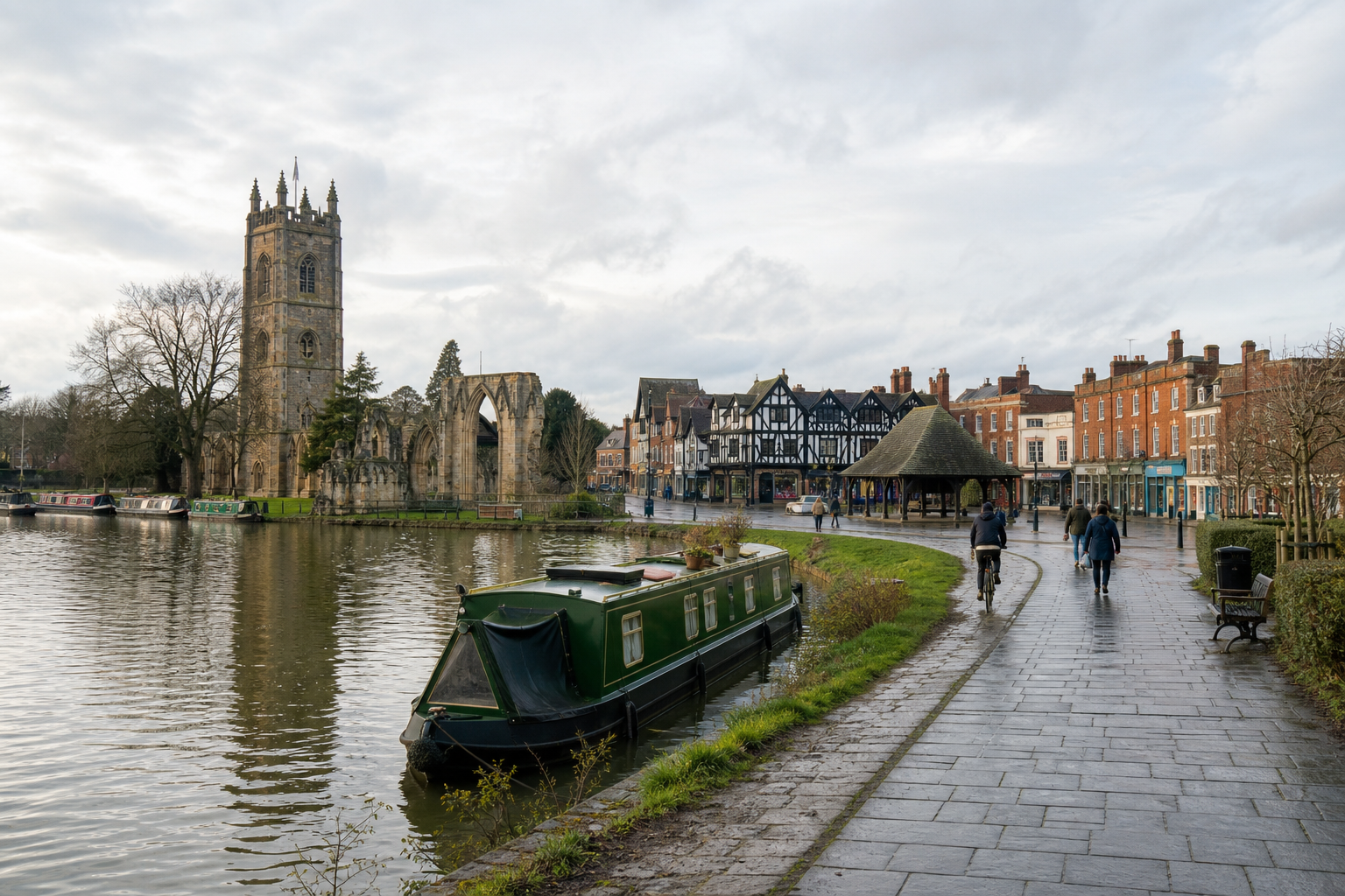 A narrowboat moored on a canal with a historic stone tower and half-timbered buildings in the background.