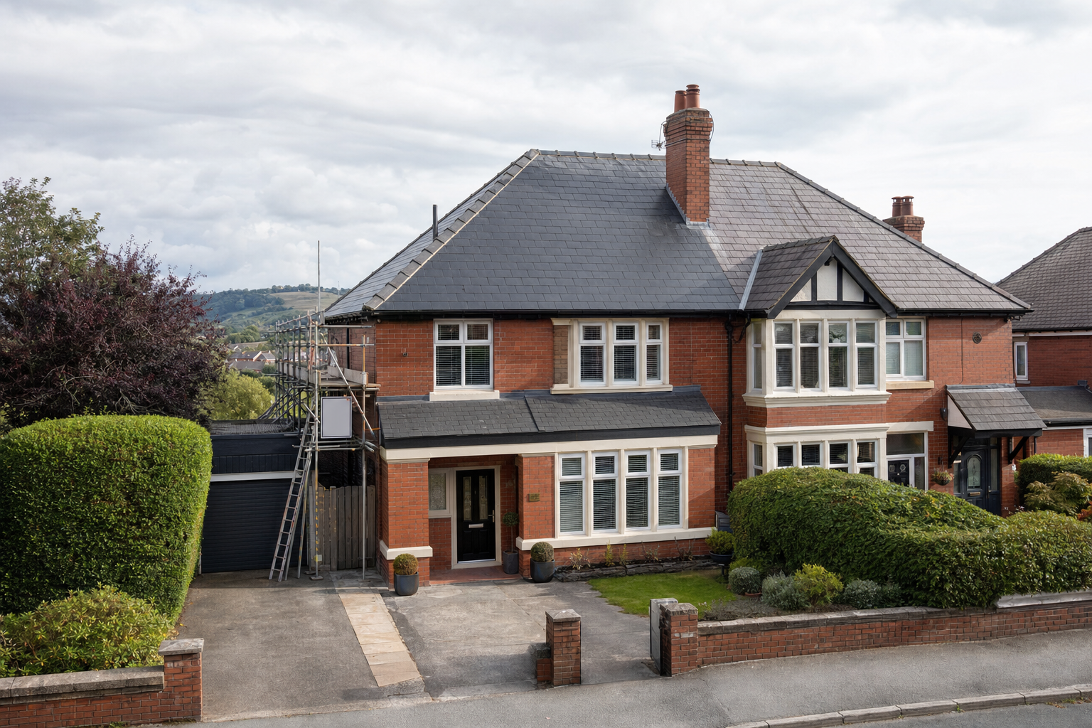 A red-brick semi-detached house with scaffolding and a ladder beside the garage, set against a rural backdrop.