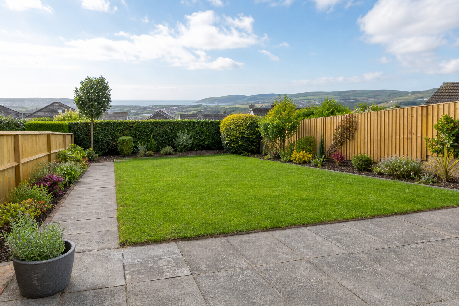 A neatly landscaped garden with a central lawn, a small tree, and surrounding wooden fences overlooking distant hills.