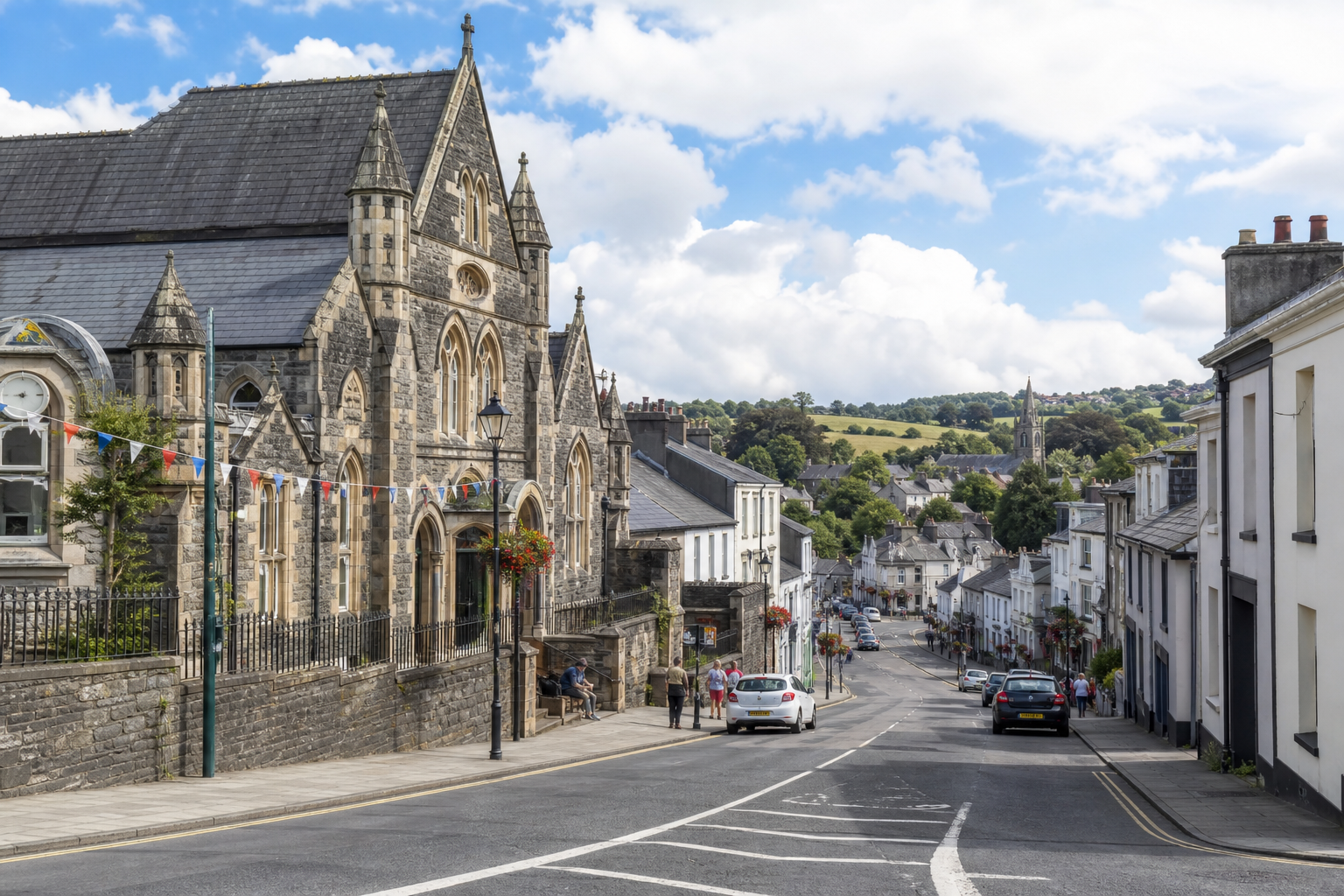 Historic stone building and street view in a quaint town with cars and greenery in the background.