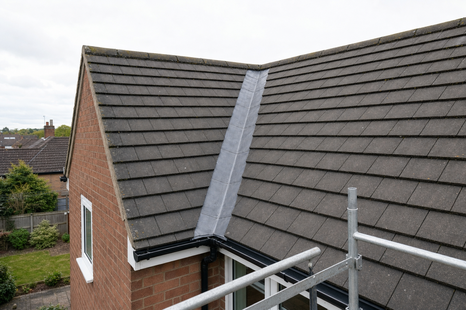 A brick house with a tiled roof and a metal valley seen from a scaffolding platform.