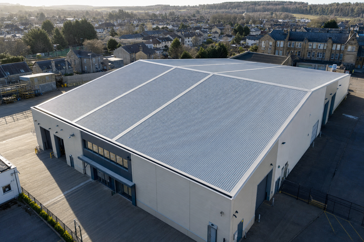 Large industrial warehouse with a corrugated metal roof set in a suburban area under a clear sky.