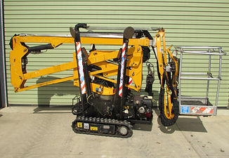 A yellow cherry picker with treads is parked in front of a green corrugated metal wall