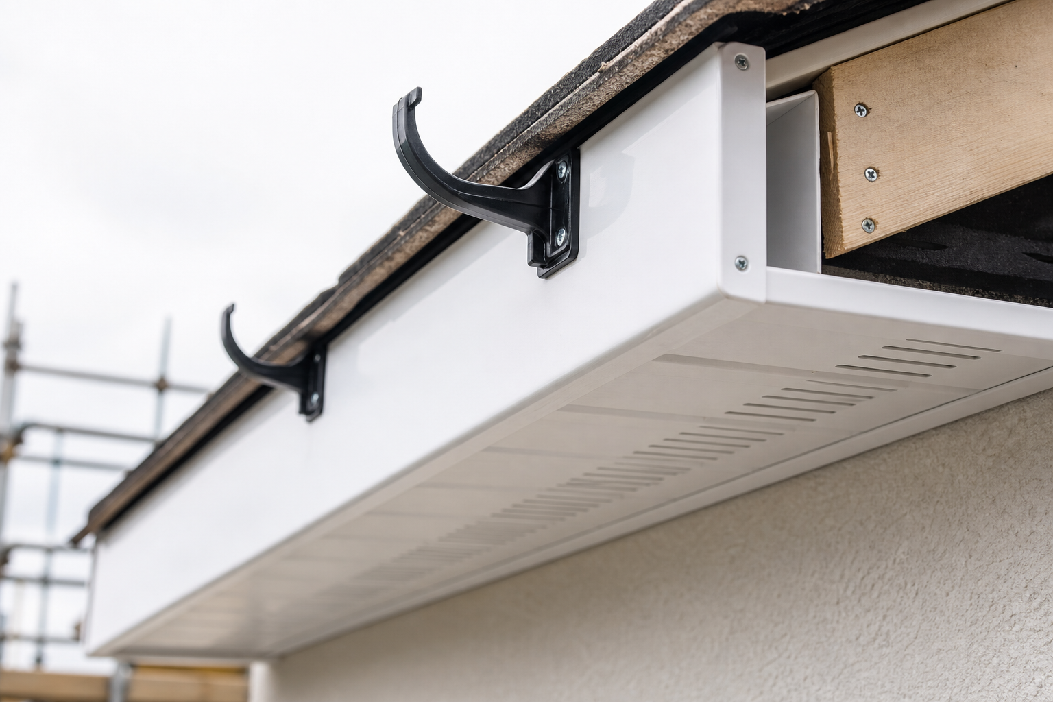 White fascia board with black brackets under a roof, partially covered by roofing felt.